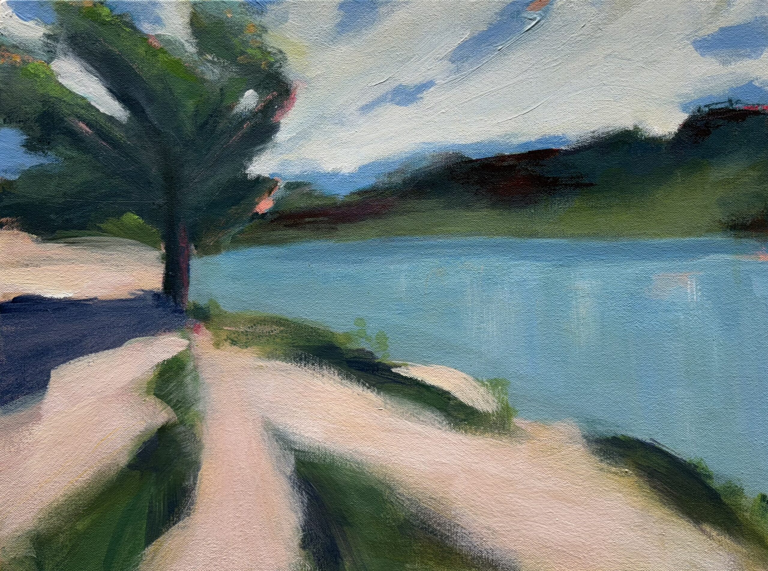 A tree bending in the wind on the light pink shoreline of a blue-green lake under a cloud swept sky.